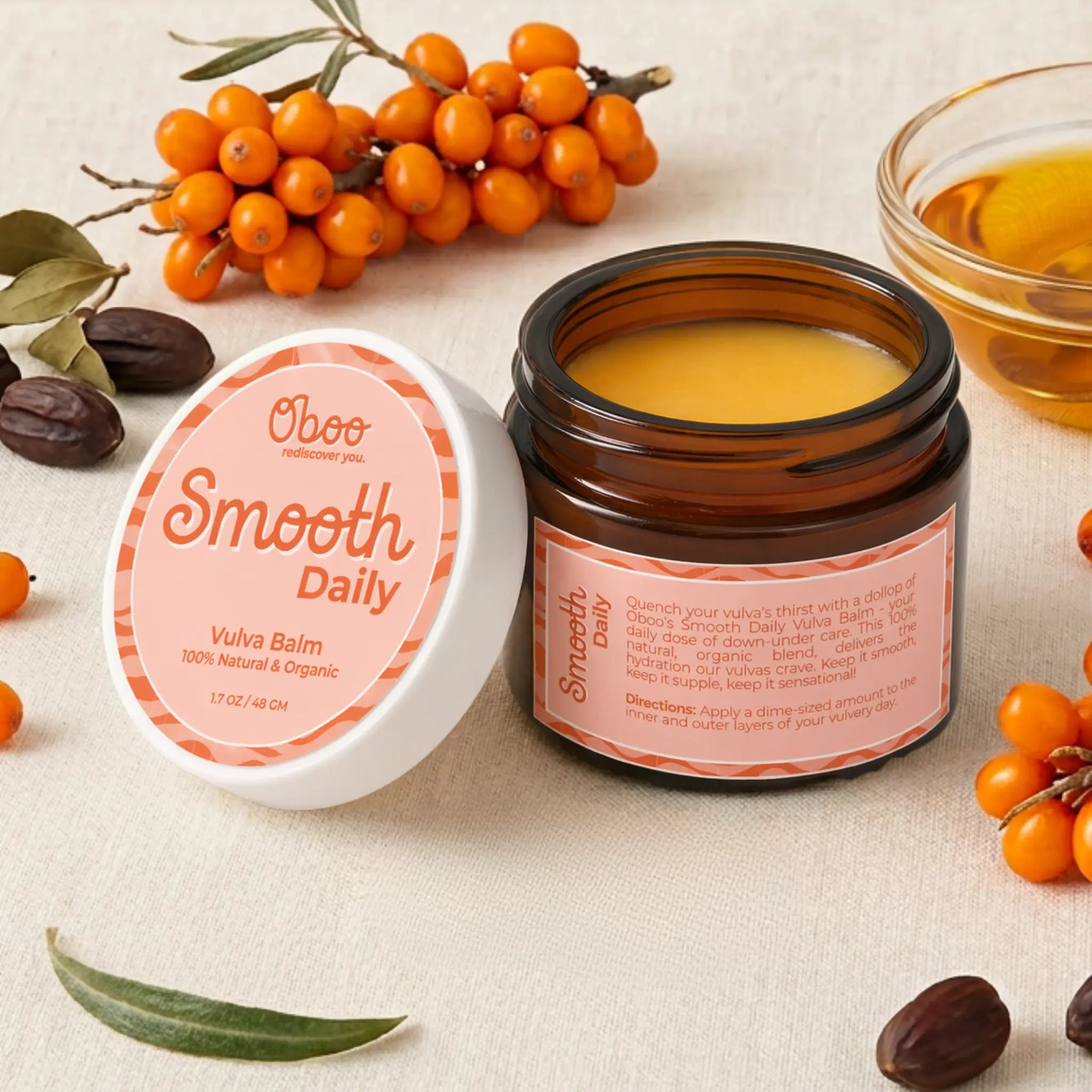 Open jar of Oboo Smooth Daily Vulva Balm beside fresh sea buckthorn berries, jojoba seeds, and a small bowl of golden oil — botanical support for soft, healthy skin