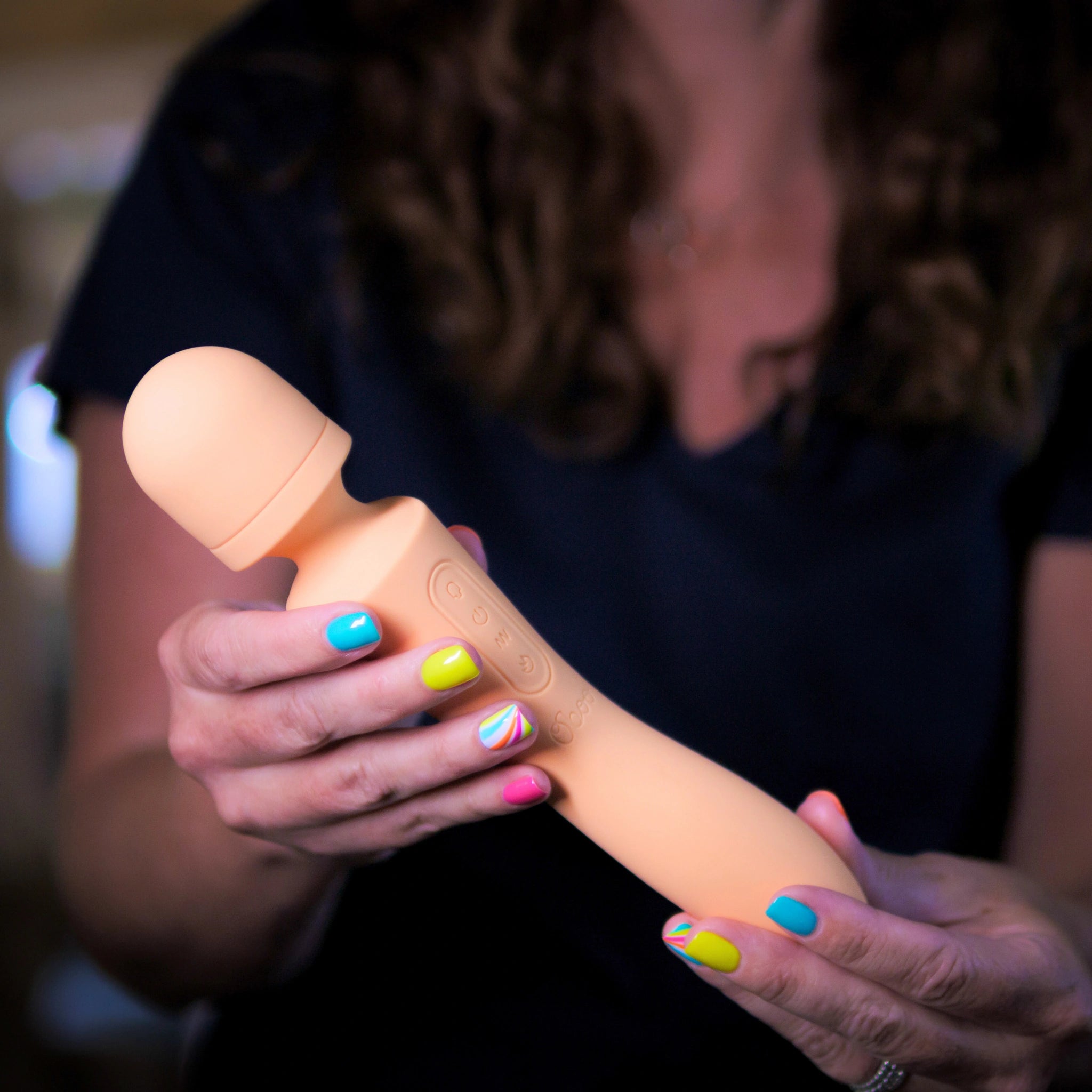 A woman holding and examining a peach-colored Boom wand massager, showcasing its ergonomic design and control buttons.