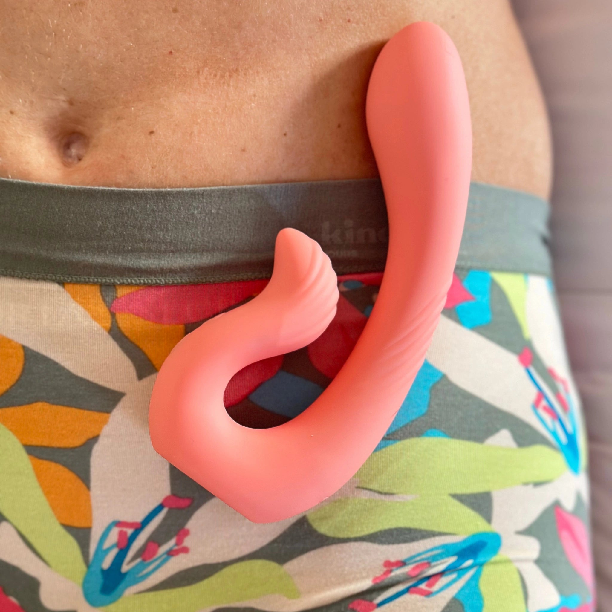 A coral-colored dual-stimulation massager rests on a person&