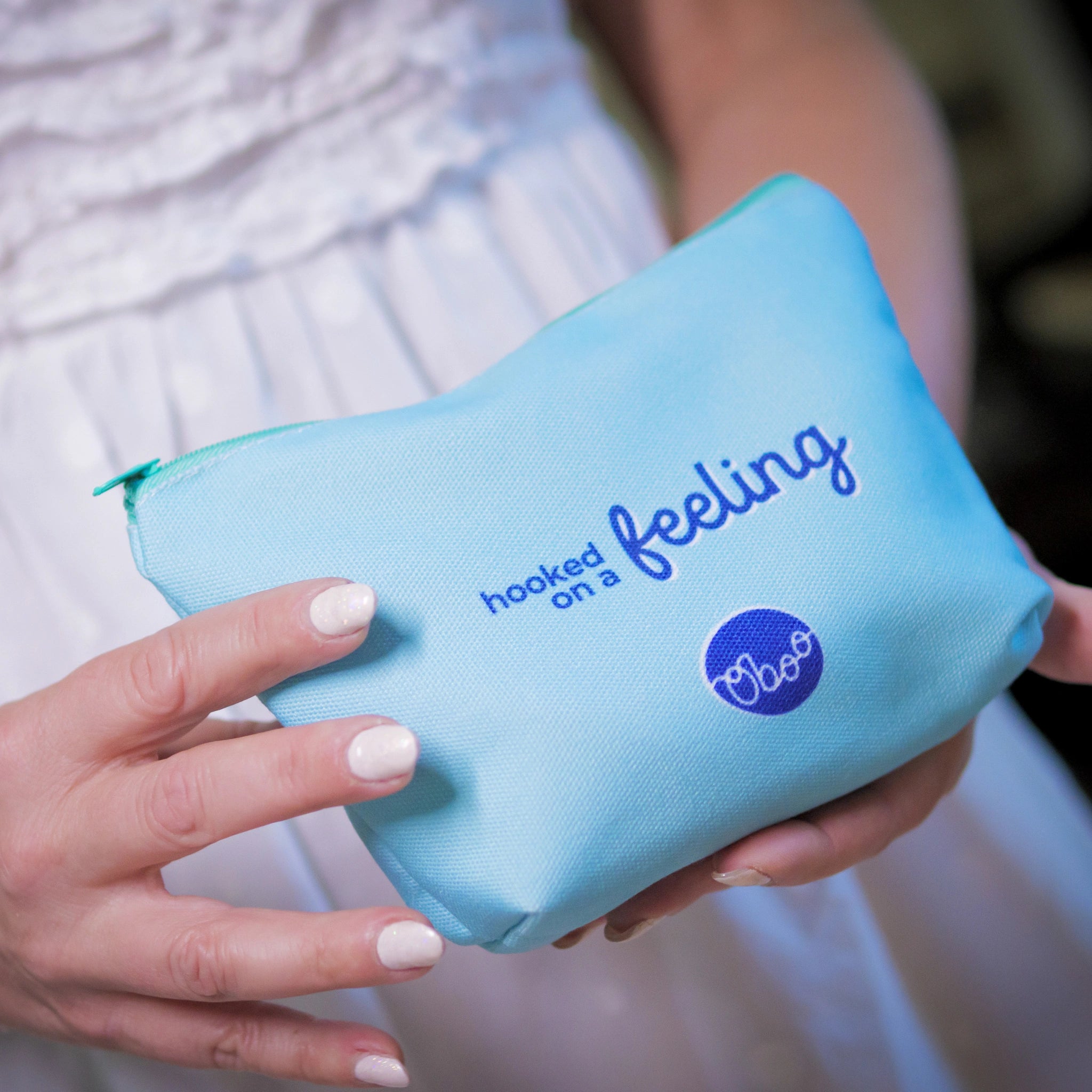 A woman in a white dress holds a light blue pouch with the words “hooked on a feeling” and the Oboo logo.