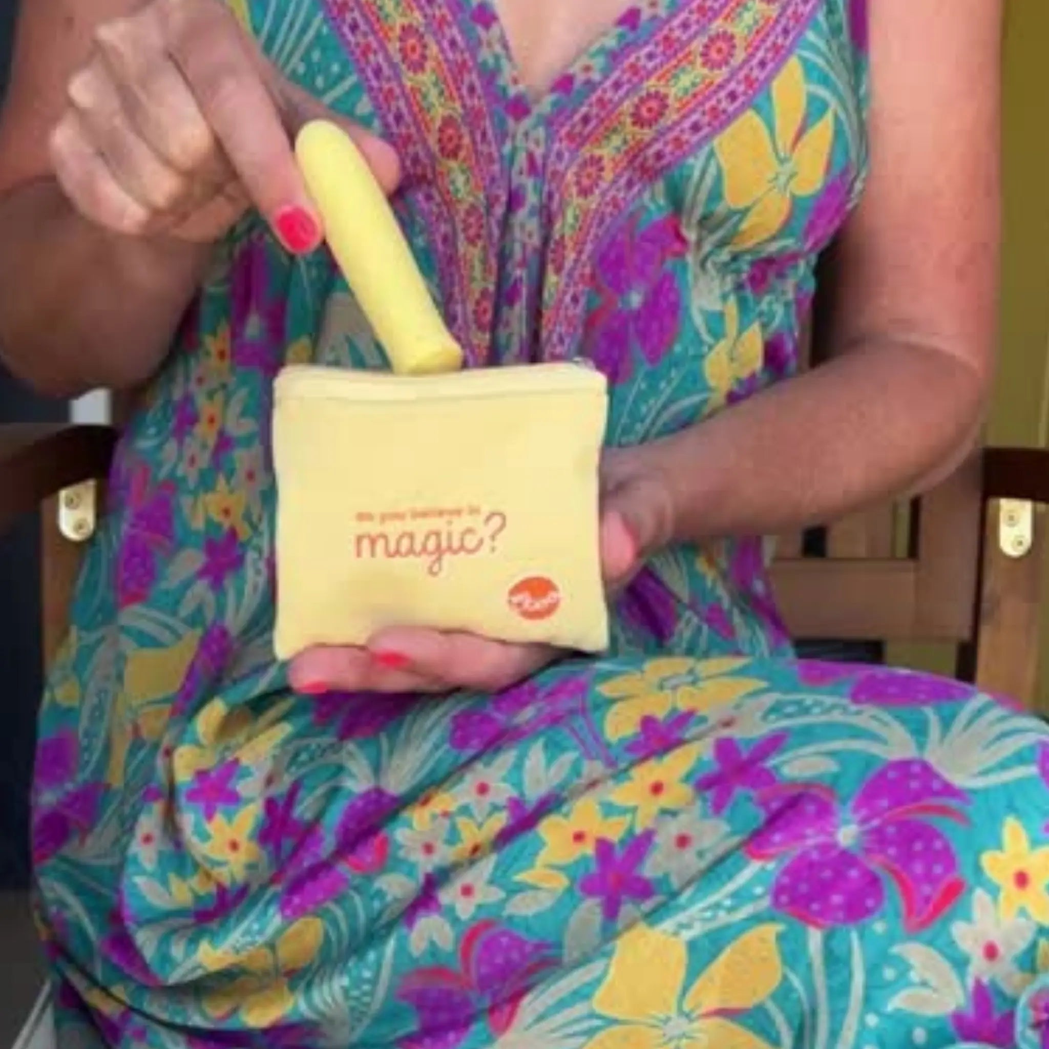 A woman in a colorful floral dress places a yellow Woo massager into a pouch labeled “Do you believe in magic?”.