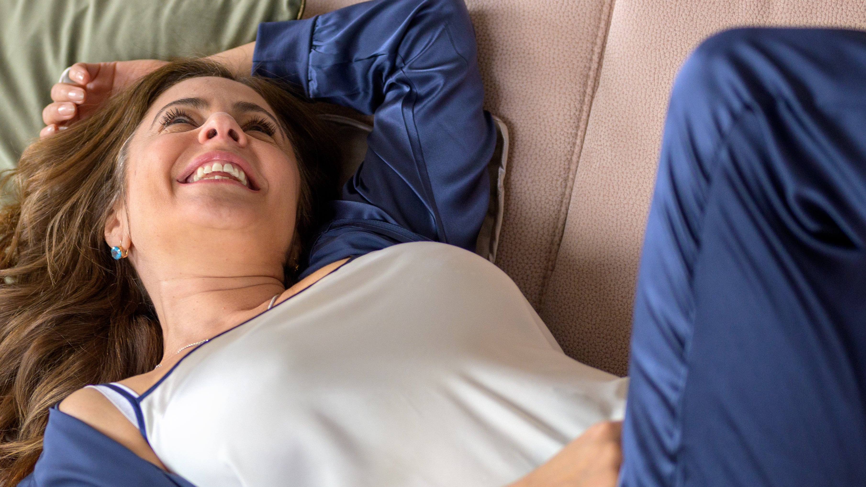 Woman lying on a couch with a pillow, wearing a blue robe and white nightgown.