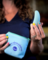 A woman with colorful nails holds a blue flexible massager in one hand and a pouch labeled “abra-abracadabra” in the other.