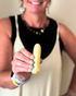A smiling woman in a cream dress holds a yellow Woo massager close to the camera, highlighting its compact, rounded design.