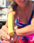 A smiling woman in a colorful outfit holds a yellow Woo massager outdoors, showing its smooth shape and branded details up close.
