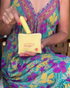 A woman in a colorful floral dress places a yellow Woo massager into a pouch labeled “Do you believe in magic?”.
