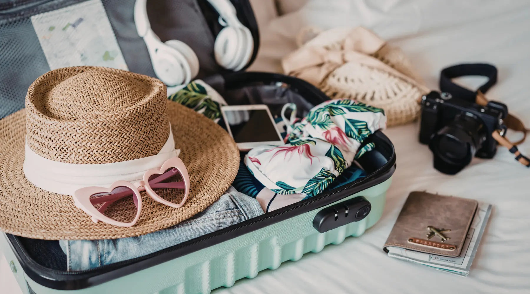 A suitcase packed with clothes, a straw hat with heart-shaped sunglasses, headphones, a camera, and a passport.