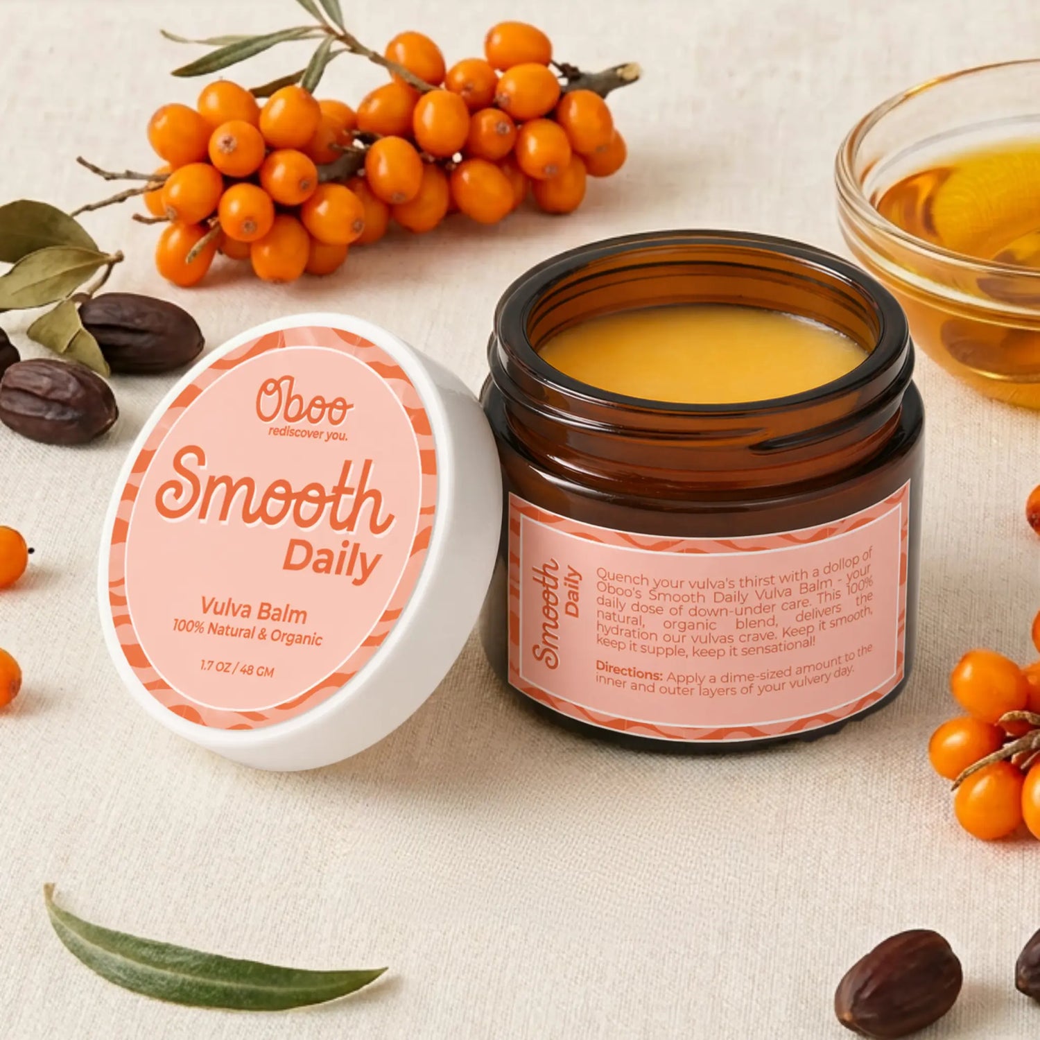 Open jar of Oboo Smooth Daily Vulva Balm beside fresh sea buckthorn berries, jojoba seeds, and a small bowl of golden oil — botanical support for soft, healthy skin