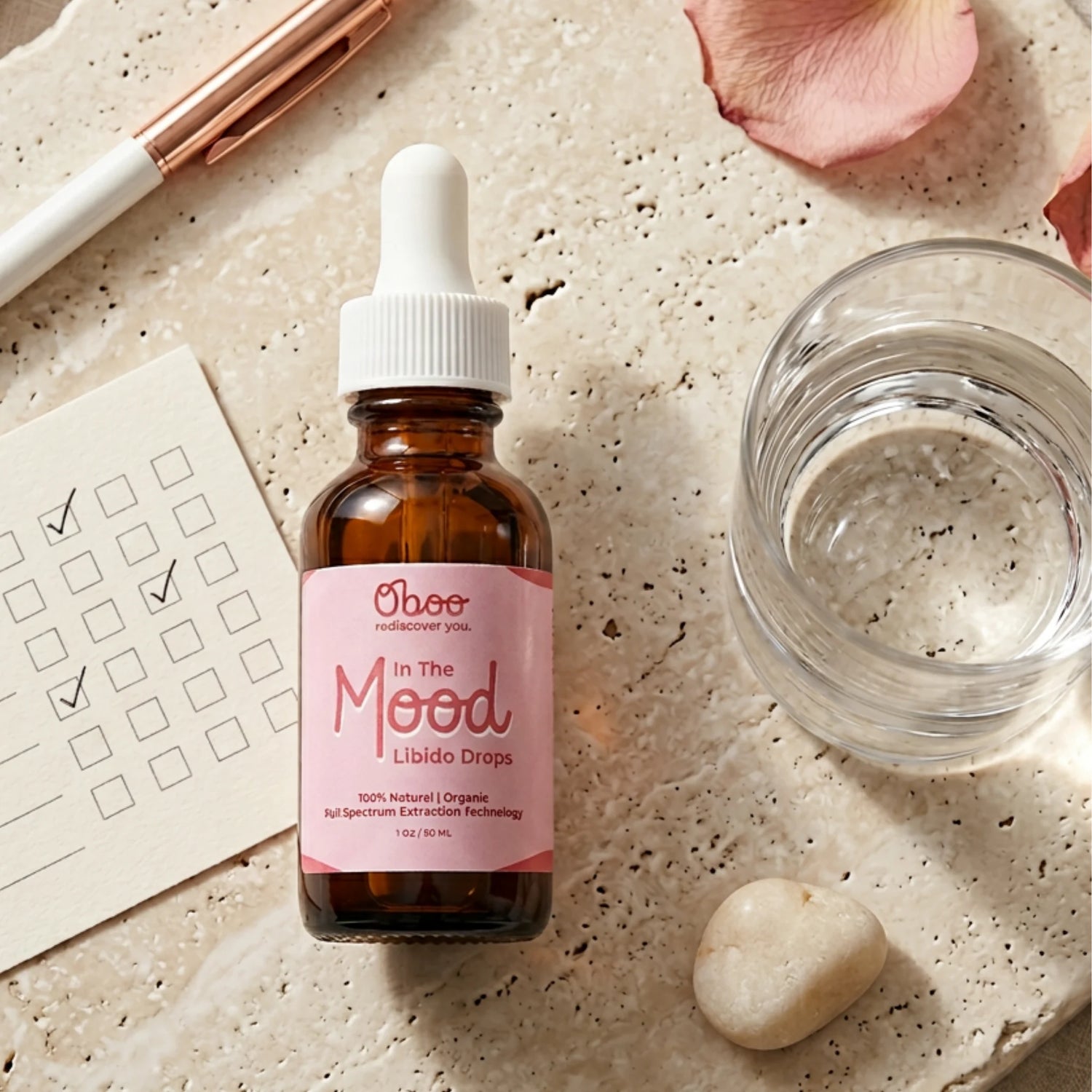 In the Mood Drops on a warm travertine surface with rose petals, a glass of water, and a daily checklist — a tiny morning ritual for midlife libido