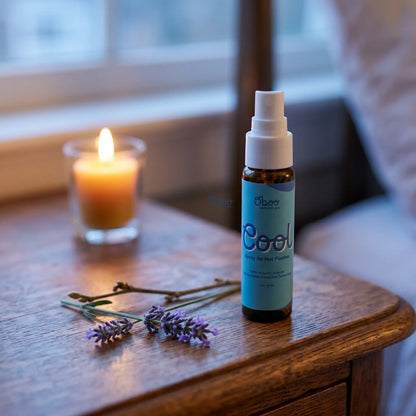 Oboo Cool Spray on a wooden nightstand beside a glowing candle and a sprig of lavender — a calming bedtime ritual for hot flashes