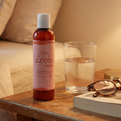 Loob Daily Moisturizer on a wooden nightstand beside a glass of water and tortoiseshell reading glasses — a gentle nightly ritual