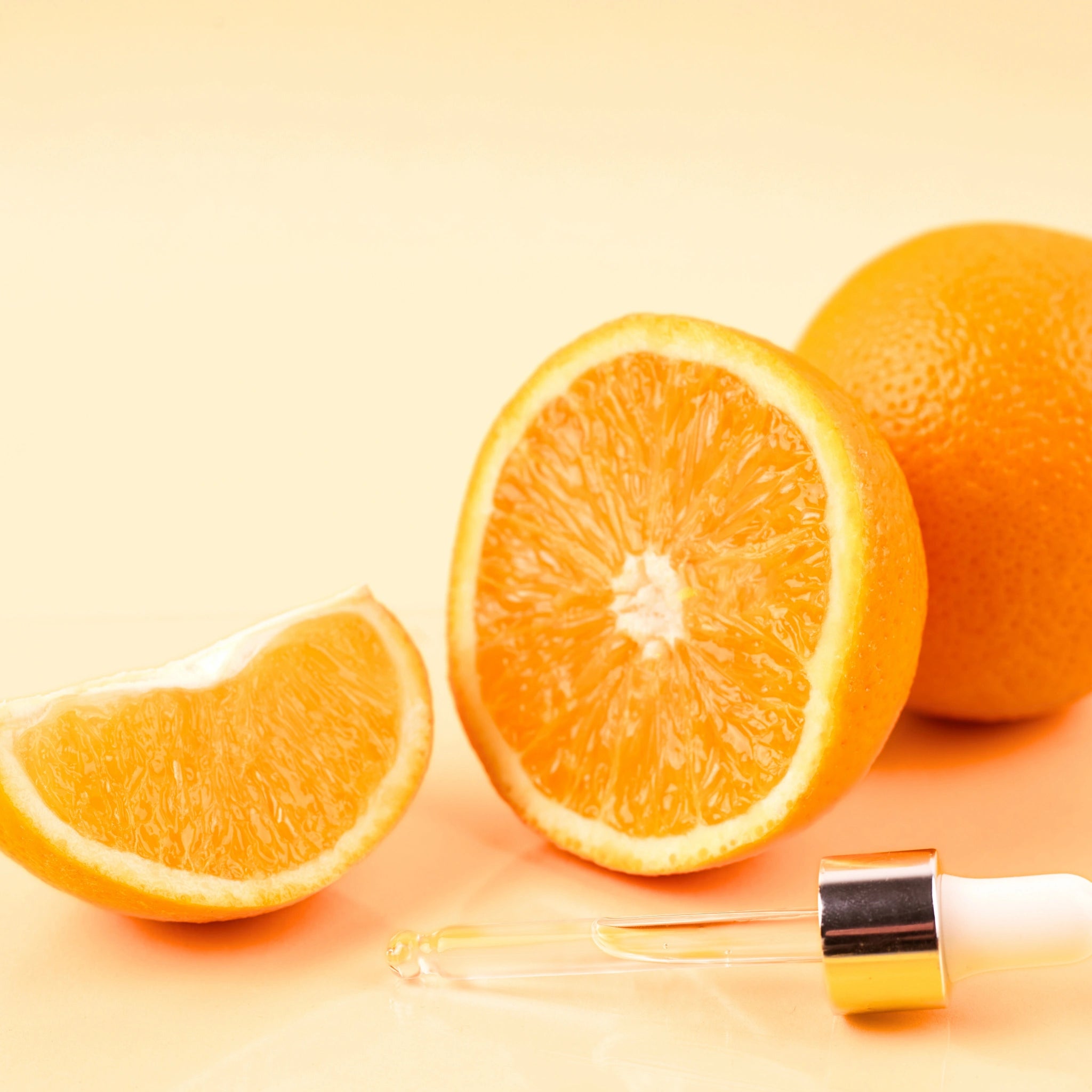 Orange slices with a dropper bottle placed on a peach background, evoking freshness, citrus scent, and natural ingredient-based skincare.