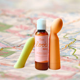 A bottle of Oboo Loob Daily lubricant is placed between two colorful massagers on a soft, blurred background of a map.