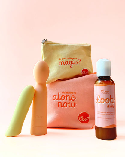 Two colorful massagers, a bottle of Oboo Loob Daily lubricant, and two pouches with playful quotes are displayed on a peach background.