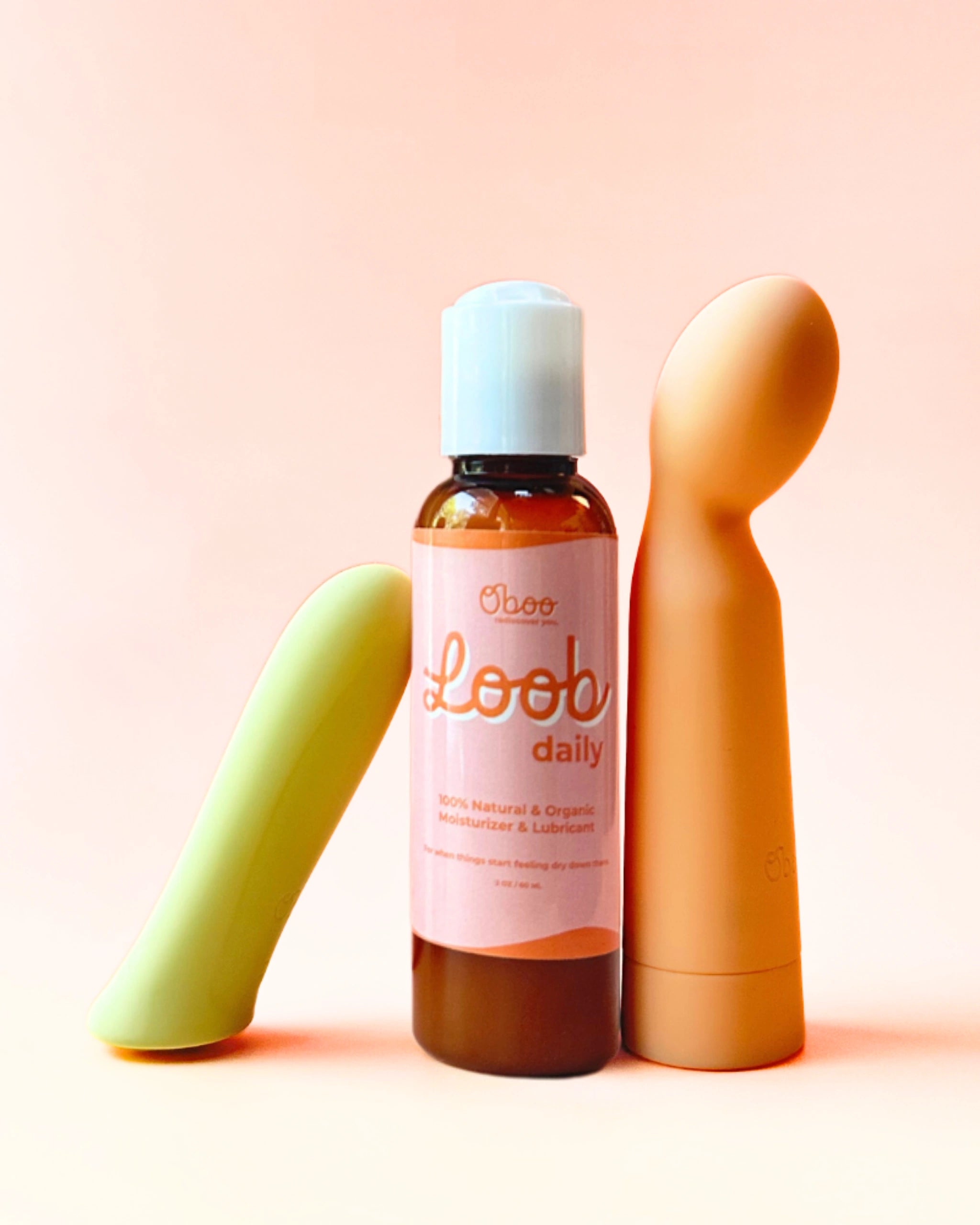 A bottle of Oboo Loob Daily lubricant is placed between two colorful massagers on a soft peach background.