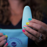 A woman with colorful rainbow nails holds a light blue flexible massager, partially visible against her chest and a blue pouch.