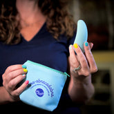 A woman with colorful nails holds a blue flexible massager in one hand and a pouch labeled “abra-abracadabra” in the other.