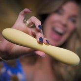 Smiling woman holding a yellow wand massager close to the camera, highlighting its curved shape and silky matte finish.