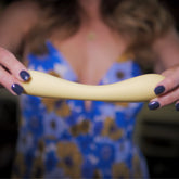 Woman in a floral dress gently bends the flexible yellow wand massager to demonstrate its soft, ergonomic design.