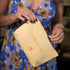 Close-up of a woman holding a pale yellow pouch that says “treat yourself,” matching the product branding.