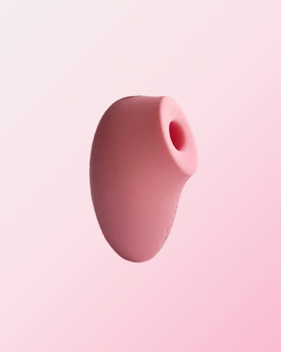 A pink silicone stimulator with a rounded body and open tip is displayed against a soft pink gradient background.